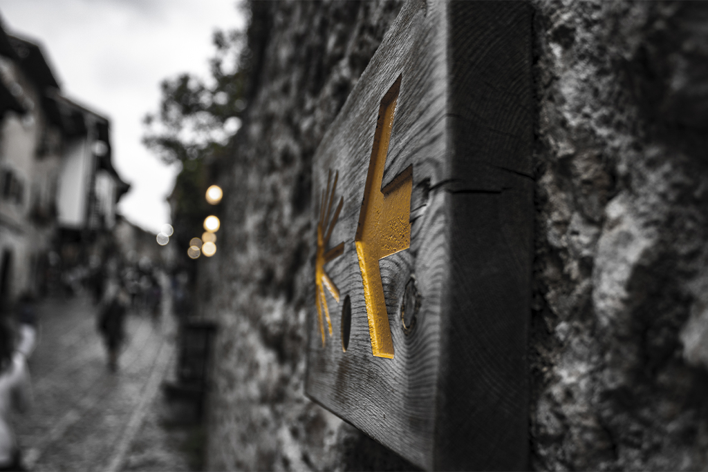Fotografía en blanco y negro dando importancia con el color a la flecha de un cartel del camino de santiago